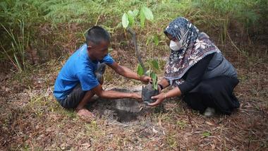 A man and a woman plant a seedling in rough soil