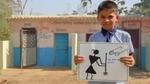 A schoolboy stands in front of a block of toilets holding a hand-drawn poster