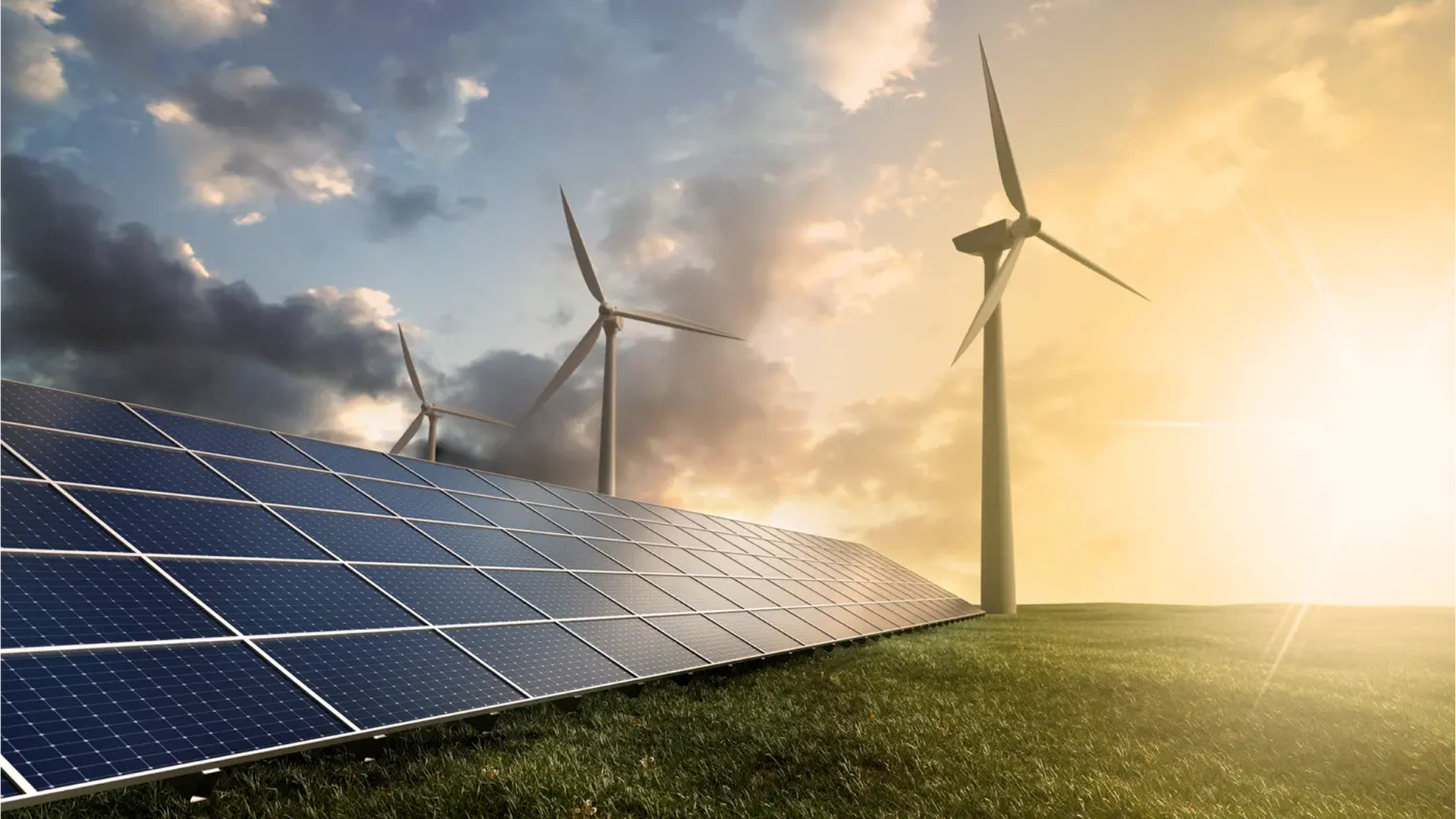 Solar panels installed on a grassy field with wind turbines in the background under a partly cloudy sky and bright sunlight.