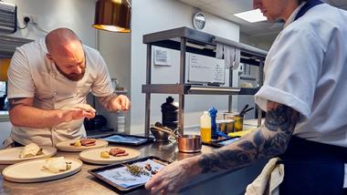 A chef puts the finishing touches to a dish while another chef looks on