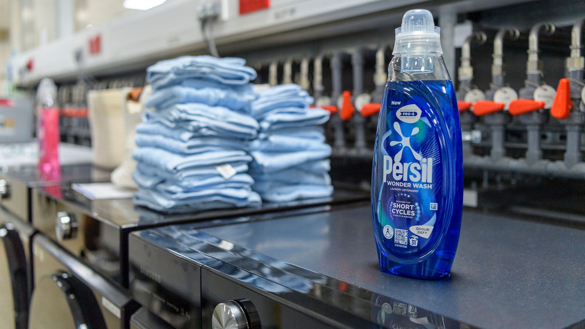 Bottles of Persil Wonder Wash and a stack of towels on top of washing machines in Unilever’s laundry detergent testing lab.