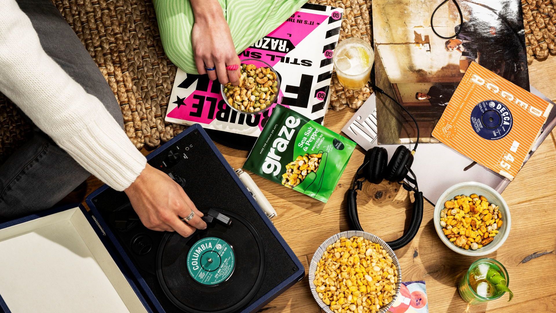 Graze snacks, a pair of headphones and a vinyl record player are placed on a wooden floor.