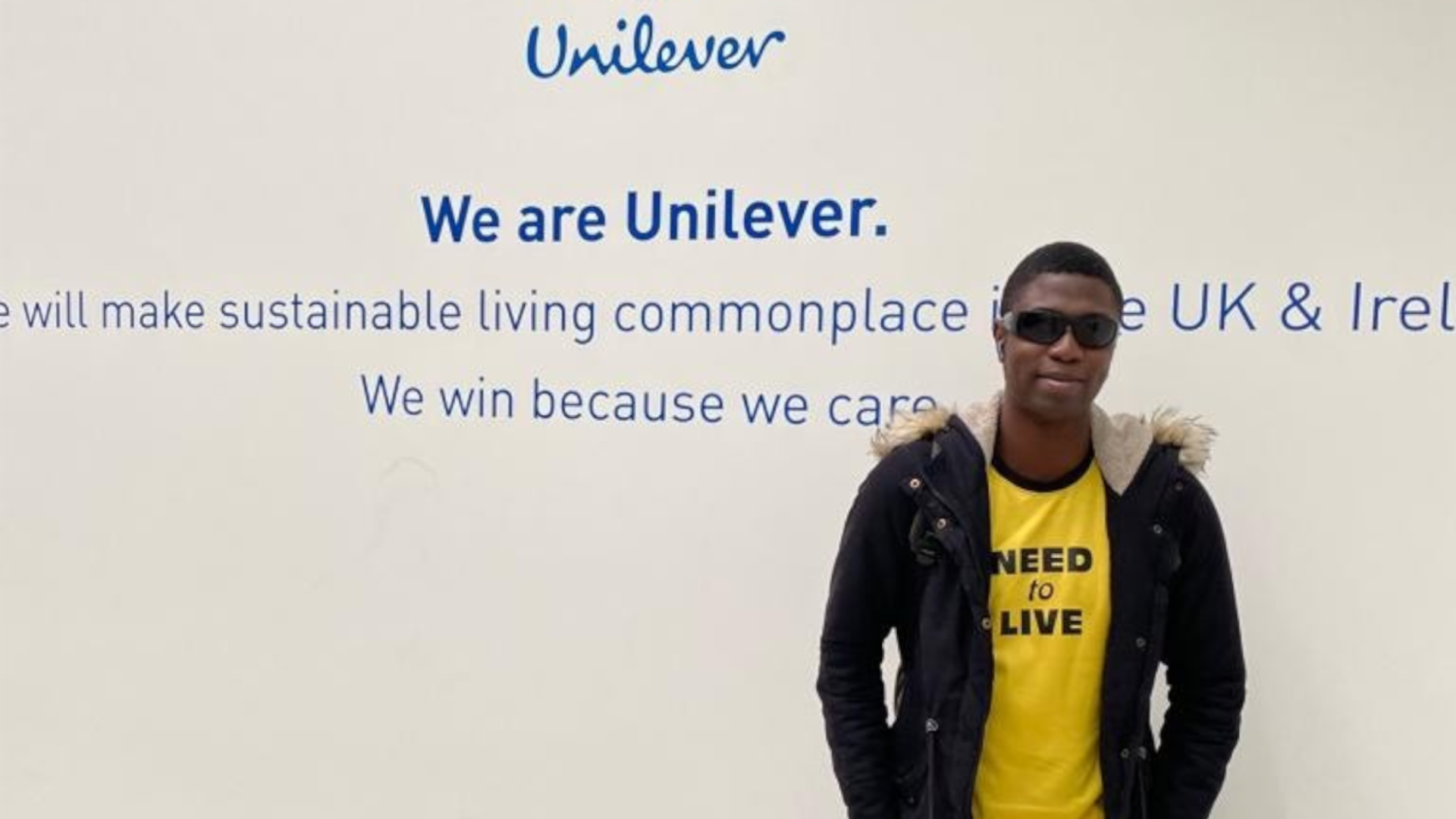 Ademola standing next to the Unilever logo on the wall inside of the Leatherhead office