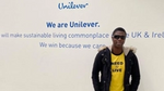 Ademola standing next to the Unilever logo on the wall inside of the Leatherhead office