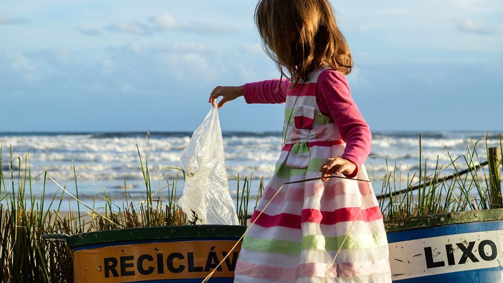 A young girl picks up a piece of plastic from some beside the sea