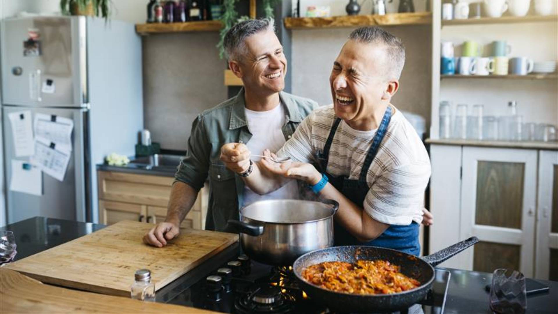 Two men laughing while cooking in a kitchen.