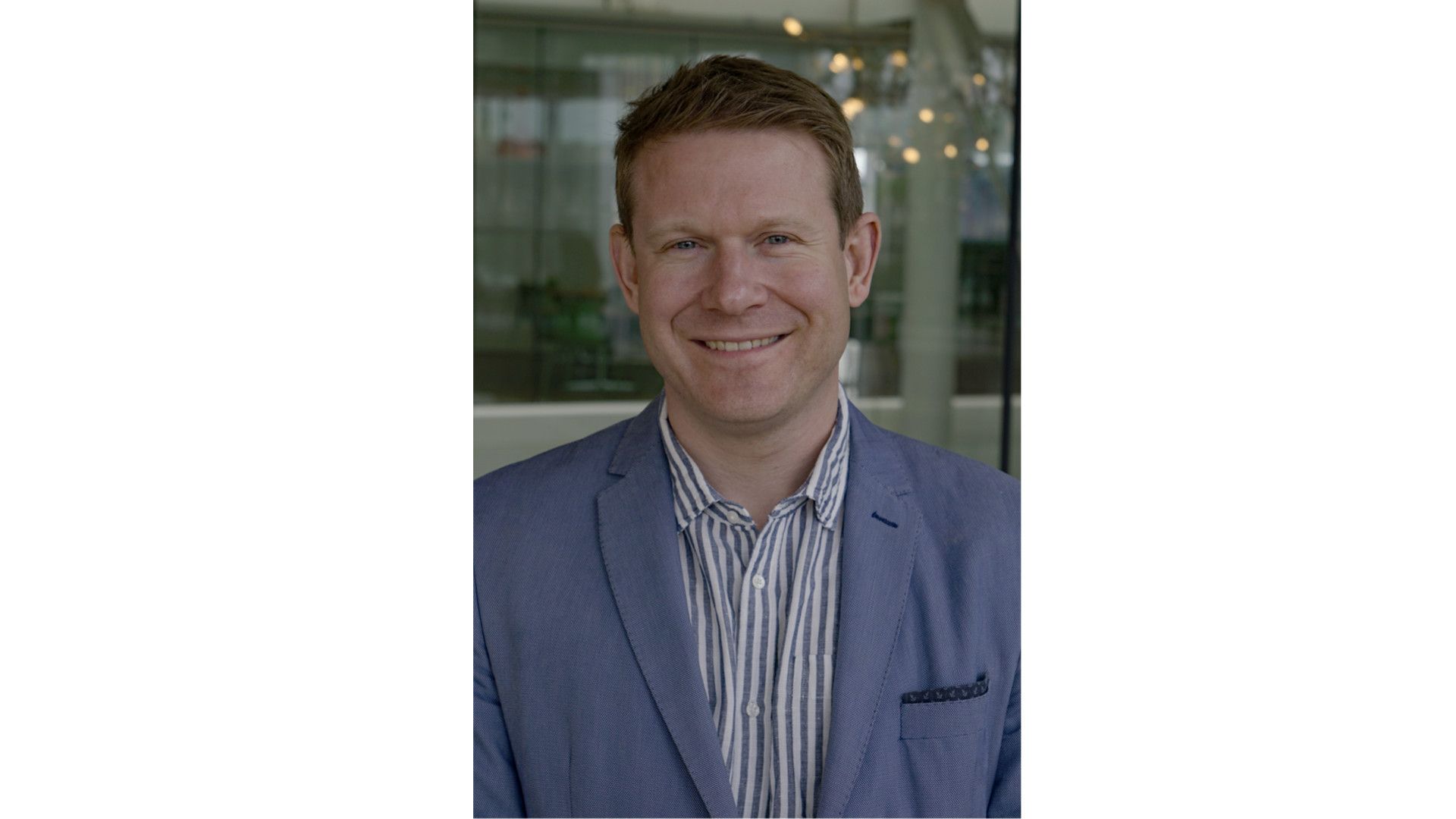 Chris Barron smiling wearing a blue blazer and striped shirt