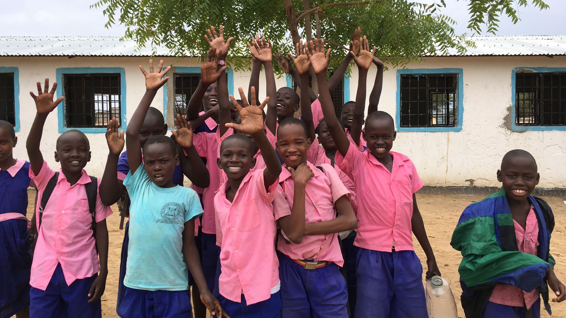 Smiling children in pink and blue shirts show their clean hands to the camera.